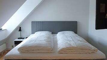 A modern bedroom with a large bed, a sloped ceiling, and a hanging light fixture.
