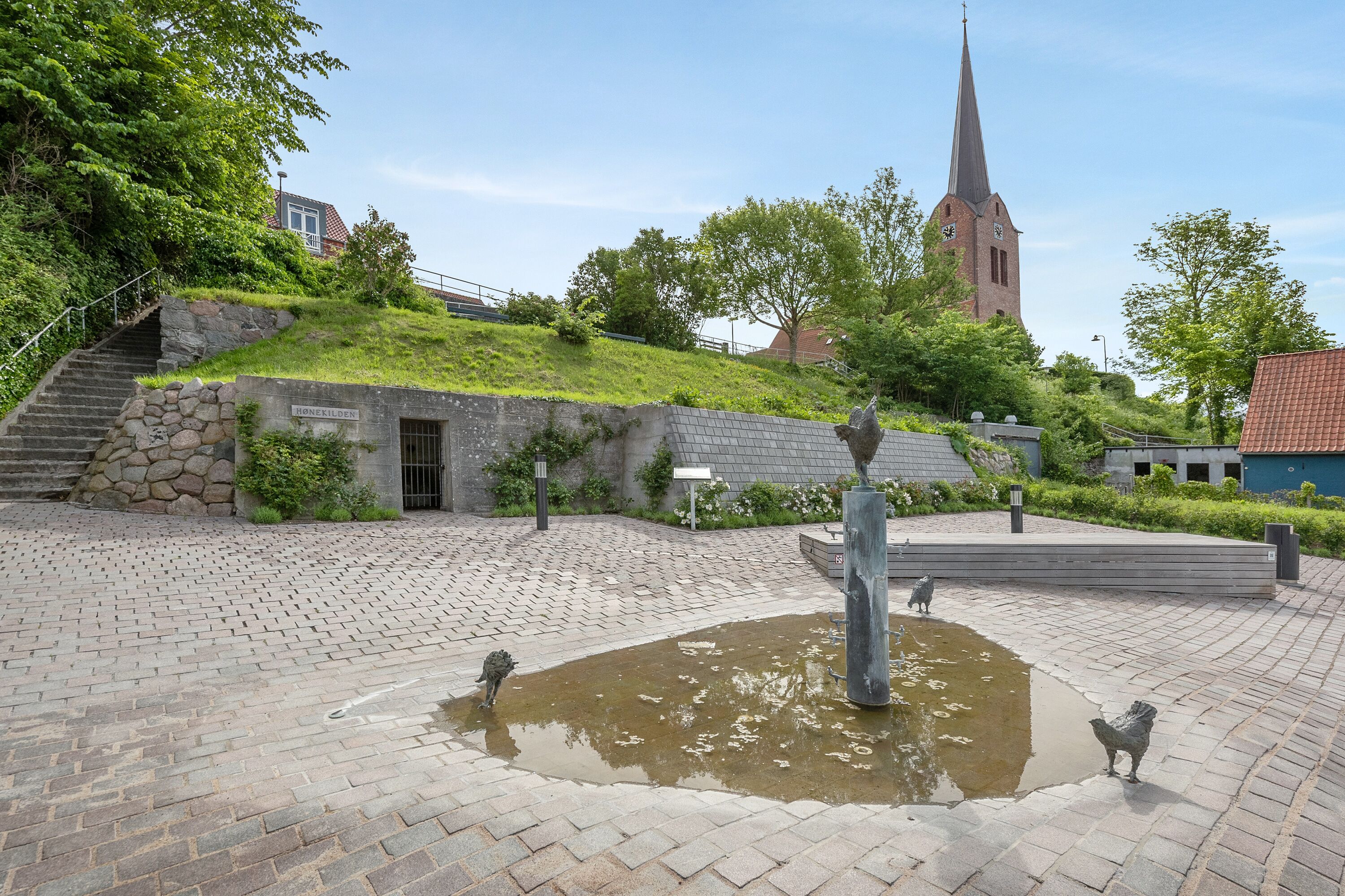 A courtyard with a stone staircase, a pond, and a church in the background.
