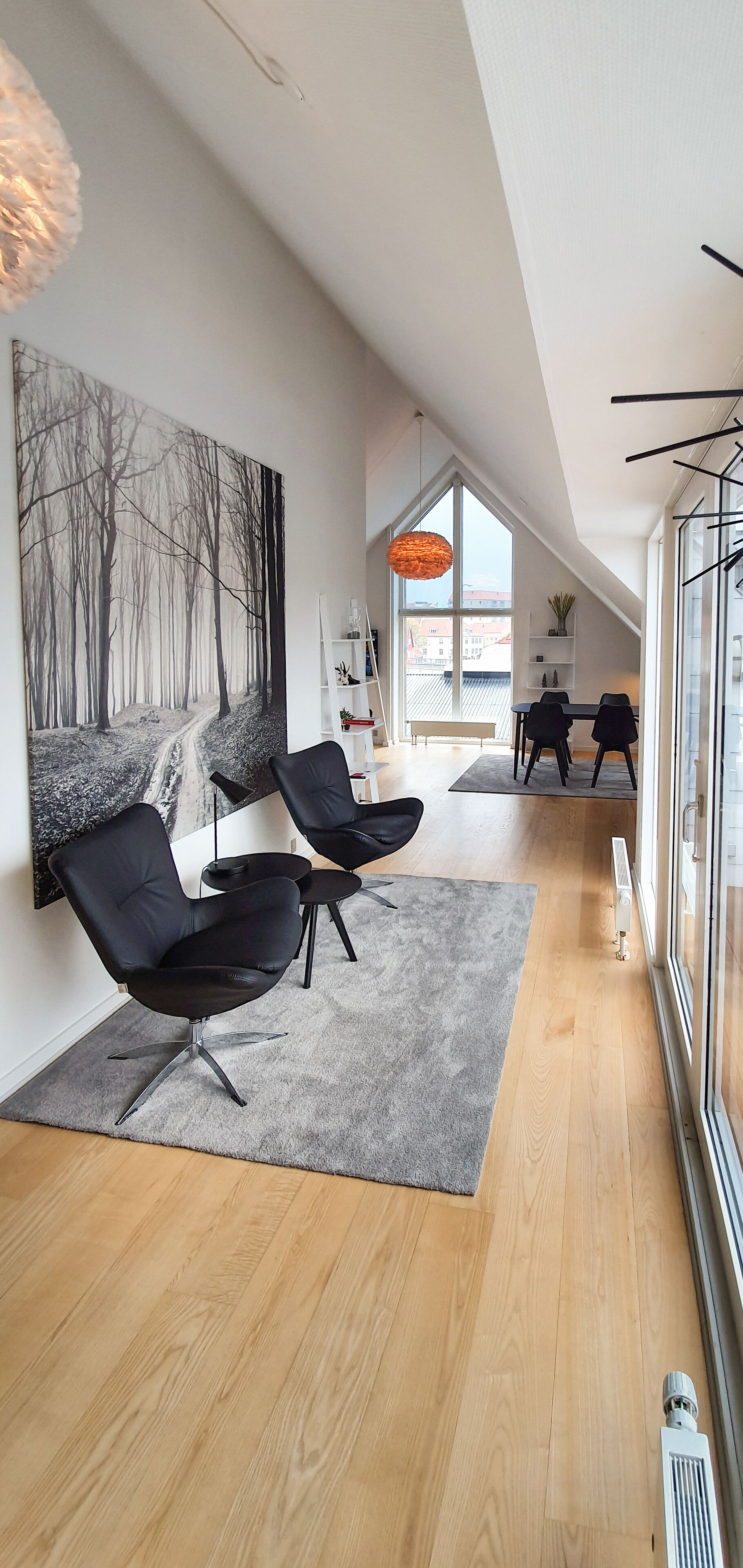 Ein modernes Interieur mit einem langen, schmalen Raum, der ein großes Fenster, einen schwarzen Ledersessel, eine weiße Regaleinrichtung und ein großes abstraktes Gemälde an der Wand zeigt.