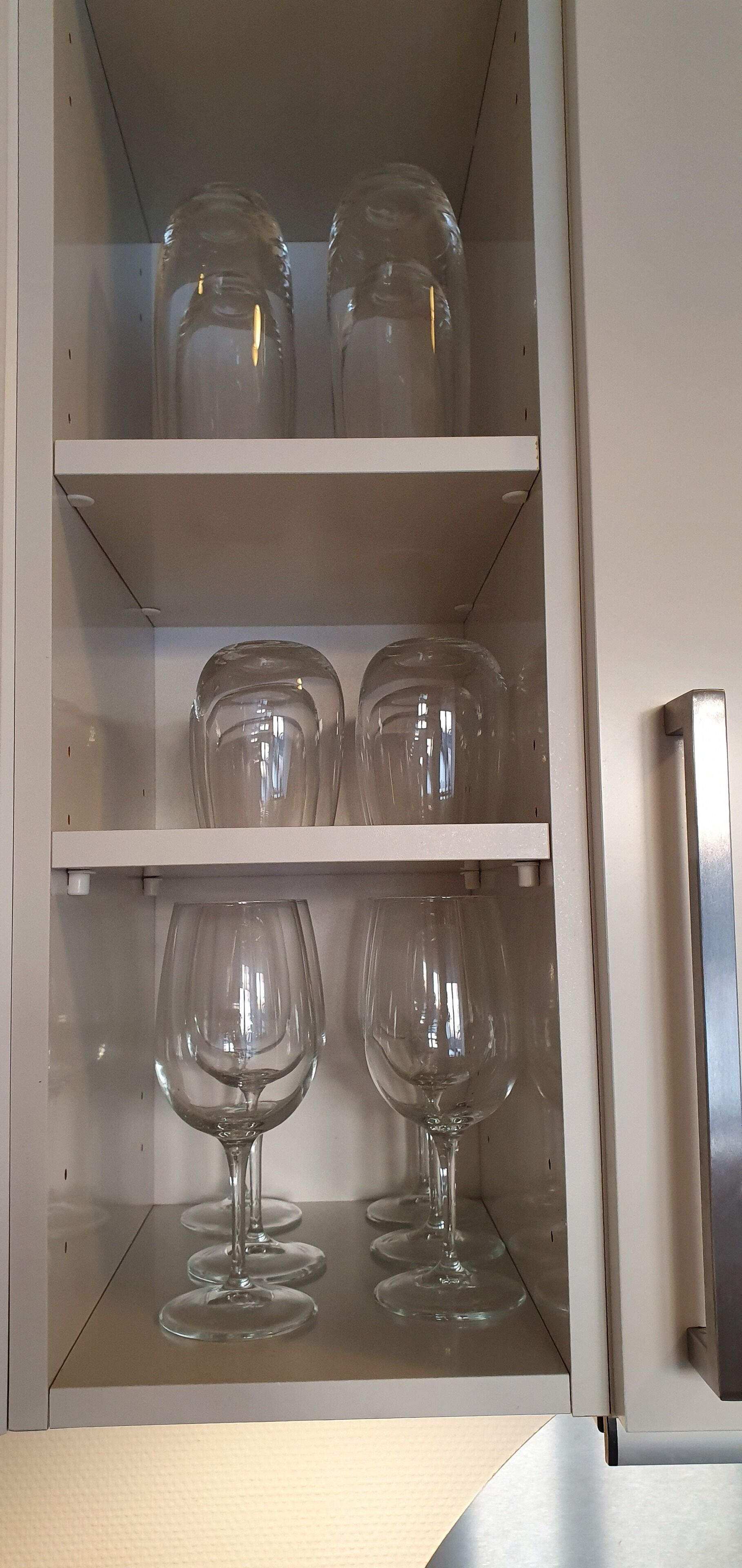 A kitchen cabinet with shelves holding clear glass jars and wine glasses.