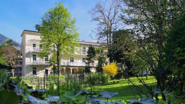 A multi-story building with balconies, surrounded by lush greenery and a well-maintained lawn.