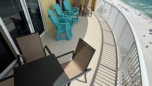Varanda com mesa e cadeiras, vista para a praia e porta de vidro que dá para uma área sombreada.