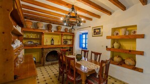 Une salle à manger rustique avec des poutres en bois, une cheminée en briques et des étagères ornées de poteries.