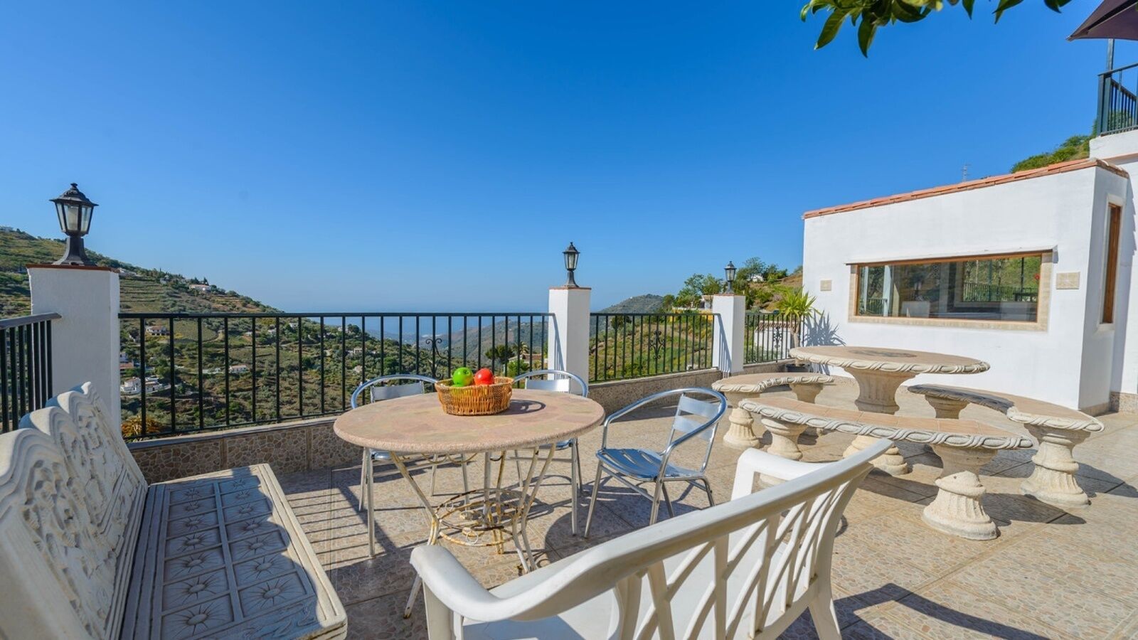 A terrace with a table and chairs, a wicker basket with fruits, and a view of the countryside.