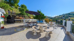 Une terrasse extérieure avec une table ronde et des chaises, entourée de plantes en pot et d’un barbecue.