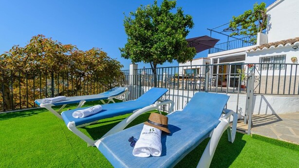Un espace aménagé au bord de la piscine, avec des chaises longues bleues, un arbre et un bâtiment doté d’un balcon.