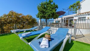 Un espace aménagé au bord de la piscine, avec des chaises longues bleues, un arbre et un bâtiment doté d’un balcon.