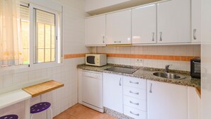 Cocina compacta con gabinetes blancos, un microondas integrado, un lavamanos y una encimera de madera.