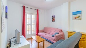 Una sala de estar con un sofá rosa, un sofá azul, una mesa de madera y un televisor sobre un soporte.