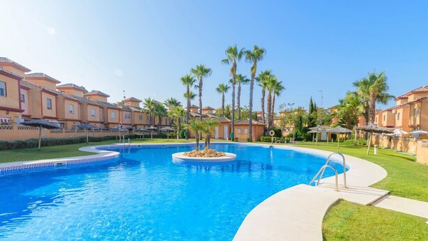Una piscina rodeada de palmeras y una hilera de edificios de estilo mediterráneo.