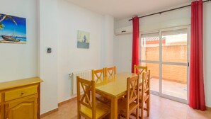 Comedor con mesa y sillas de madera, un mueble bajo y un ventanal corredero que da a un espacio exterior.