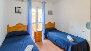 Una habitación con dos camas, un aparador de madera y una ventana con cortinas azules.