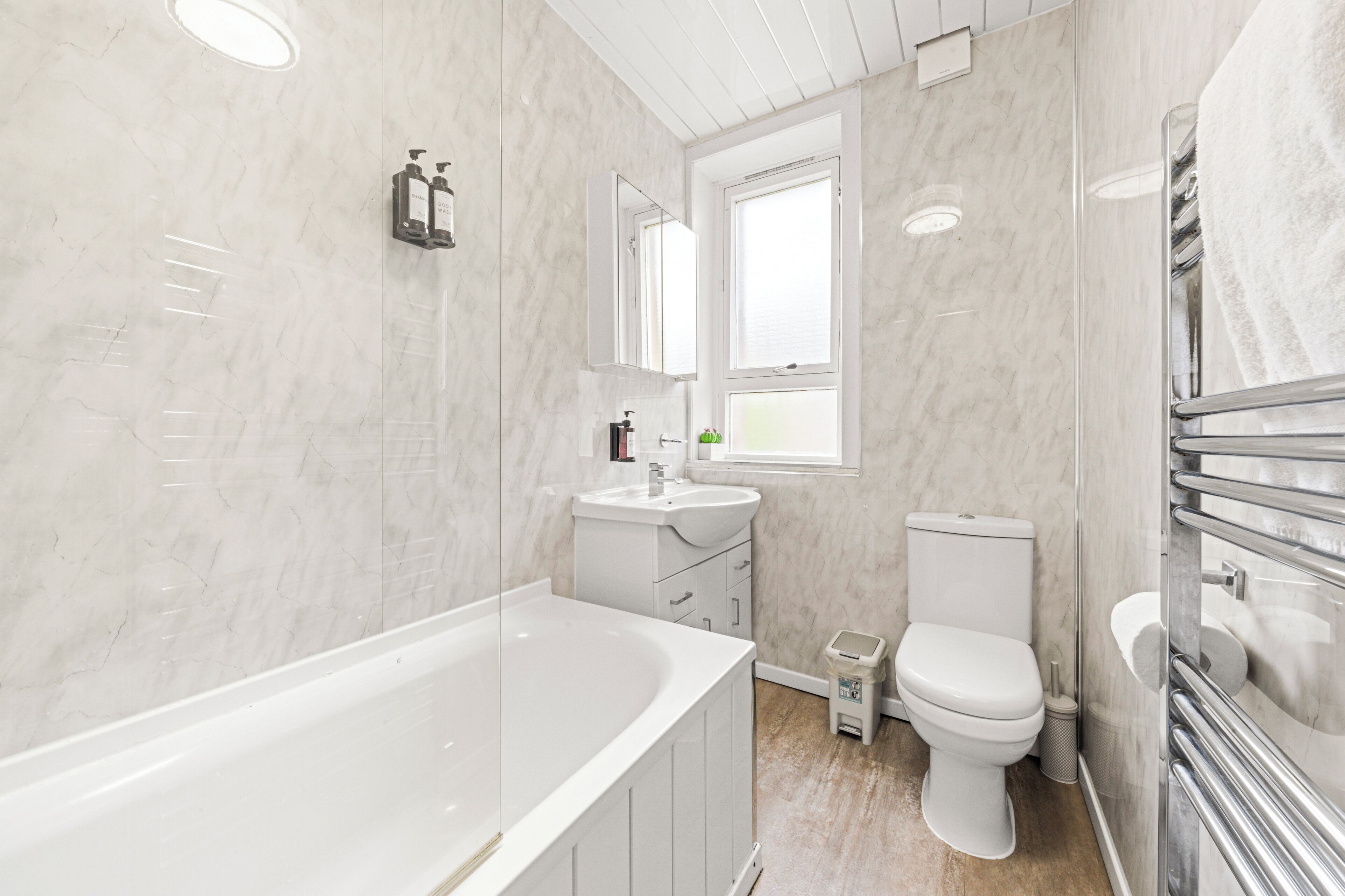 Een moderne badkamer met een bad, wastafel, toilet en een raam dat voor natuurlijk licht zorgt.