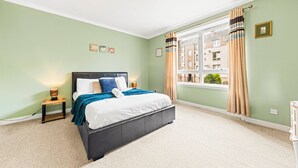 Un dormitorio con cama, mesitas de noche, una ventana con cortinas y vistas a edificios.