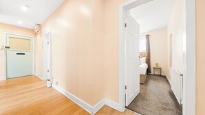 Habitación de hotel con piso de madera, una puerta que da a un baño y una pequeña mesa con lámpara.