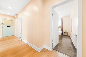 Habitación de hotel con piso de madera, una puerta que da a un baño y una pequeña mesa con lámpara.
