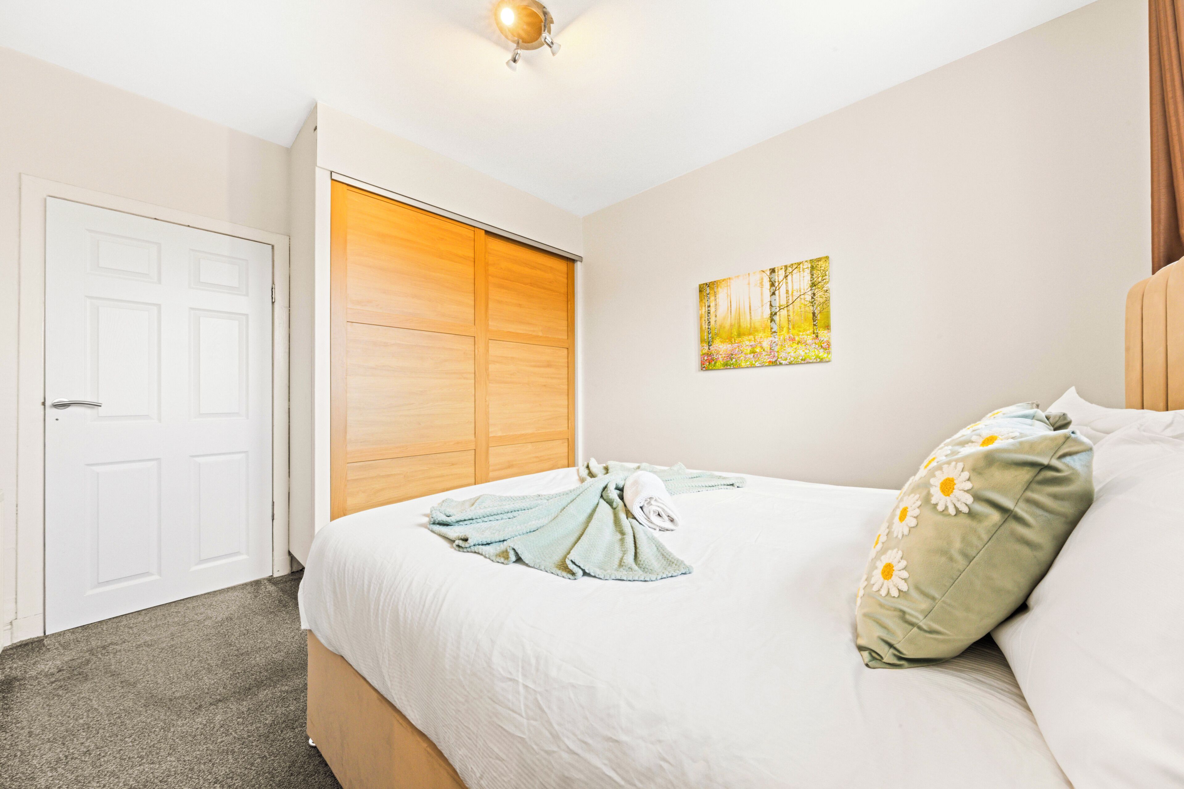 A bedroom with a bed, a wooden wardrobe, a white door, and a painting on the wall.