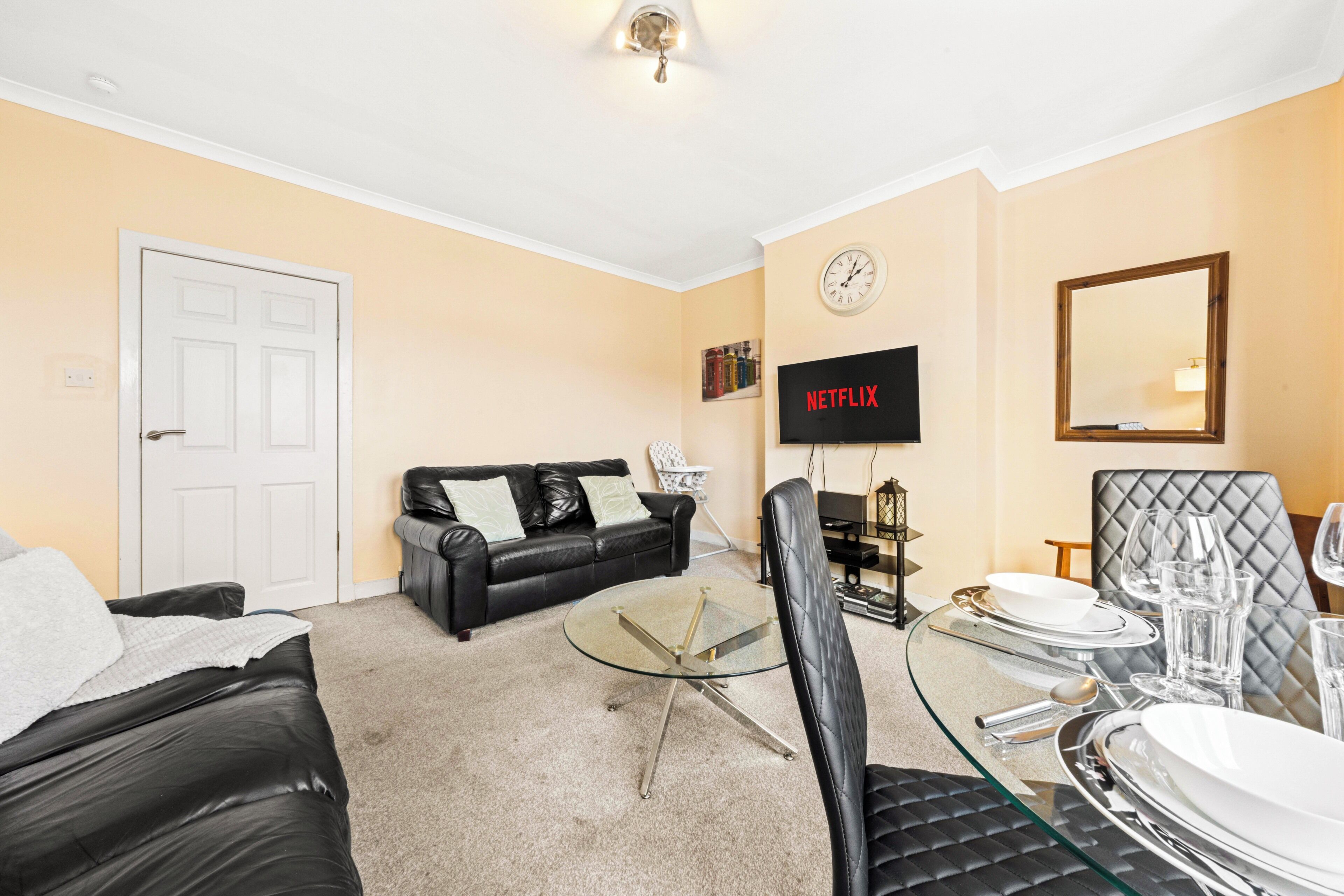 A living room with a glass coffee table, black leather sofa, and a dining area with a glass table and chairs.