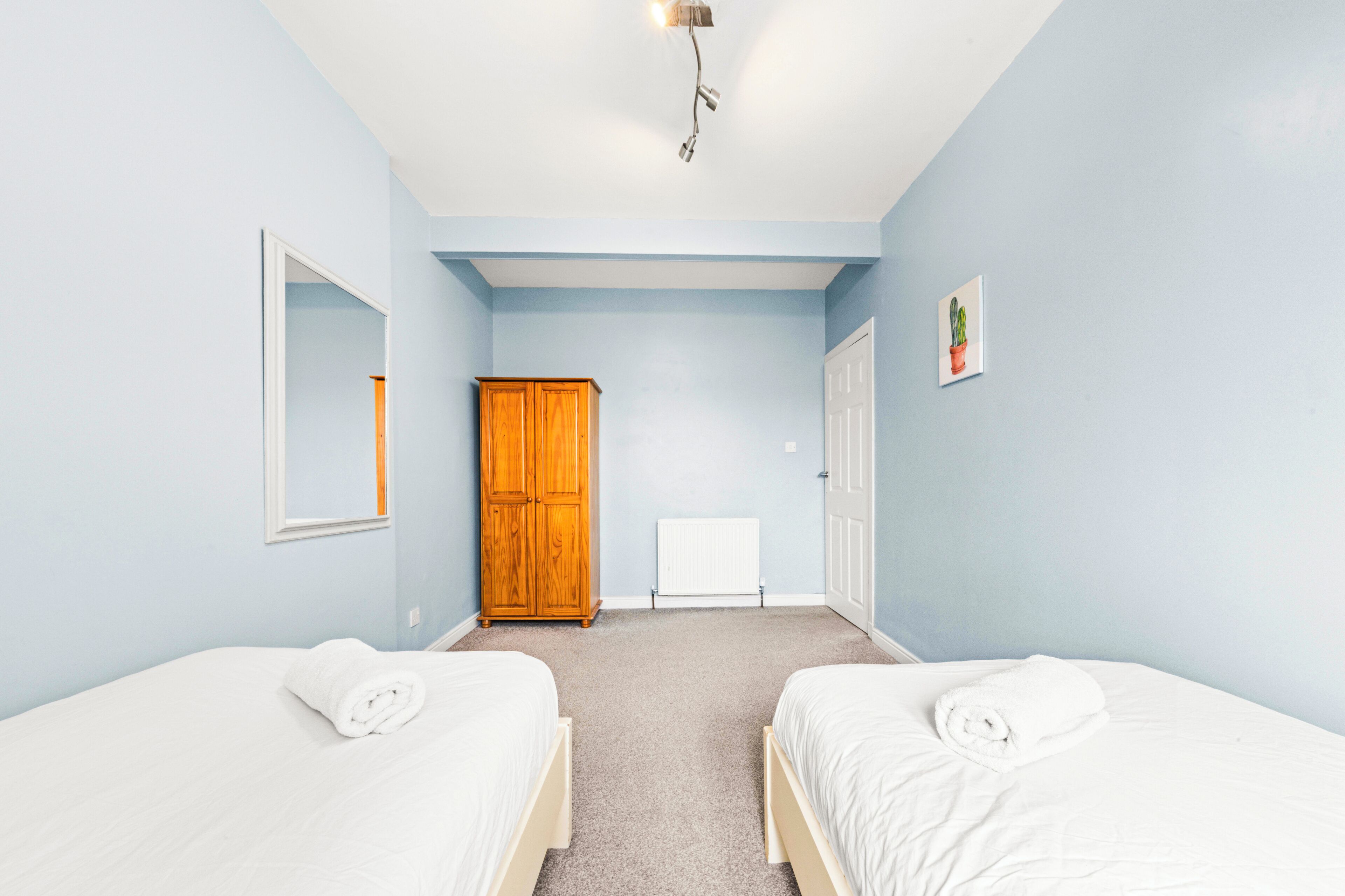 A bedroom with two beds, a wooden wardrobe, a radiator, and a ceiling light fixture.
