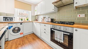 Una cocina moderna con armarios blancos, encimera de madera, horno integrado, microondas y lavadora.