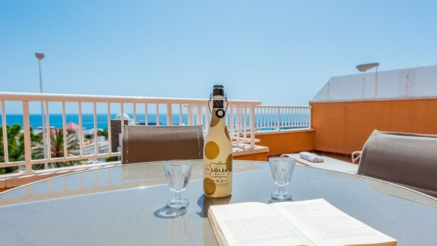 Una mesa con una botella de vino Brut Lolei, dos copas y un menú abierto en un balcón con vista al mar.