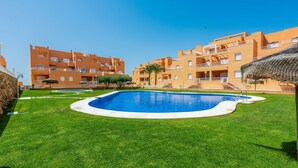 Una piscina rodeada de césped cuidado, con edificios de apartamentos anaranjados al fondo.
