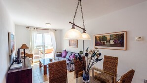 Una sala de estar moderna con comedor, que presenta mobiliario de mimbre, una lámpara colgante y un amplio ventanal con cortinas.