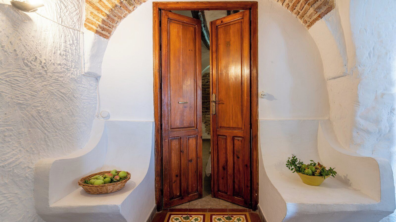 A doorway with wooden doors, a basket of green apples, and a bowl of fruit on either side.