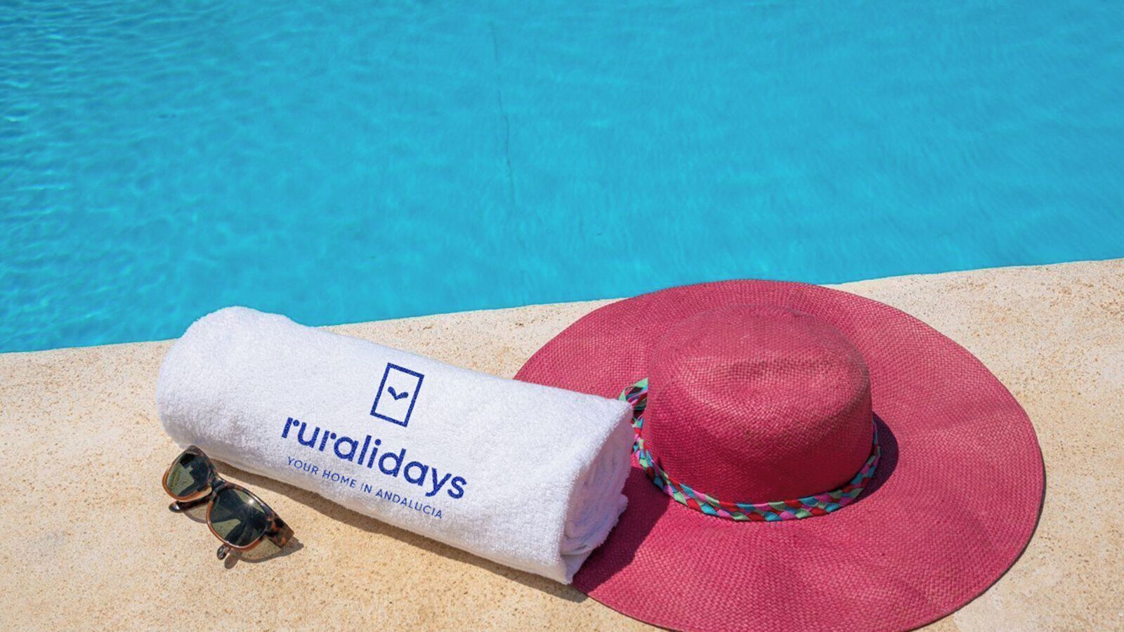Une serviette, des lunettes de soleil et un chapeau rouge, près d’une piscine.