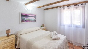 A bedroom with a bed, a nightstand, a lamp, a painting, and a window with curtains. - Villa Sol Alozaina by Ruralidays (Málaga)