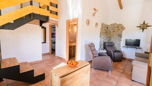 A spacious living area with a wooden staircase, a stone wall, and a television. - Villa Sol Alozaina by Ruralidays (Málaga)