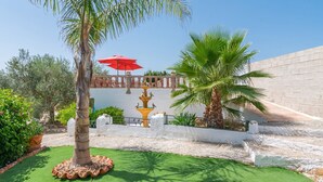 A courtyard with a palm tree, a fountain with birds, a red umbrella, and a white wall. - Villa Sol Alozaina by Ruralidays (Málaga)