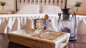A wooden tray with glassware and a candle on a wooden table in a bedroom with a bed and a nightstand in the background.