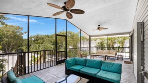 A spacious balcony with a teal sofa, a glass coffee table, and a ceiling fan. - Beachfront Hideaway in the heart of Key Largo! Your own private beach! (Key Largo)
