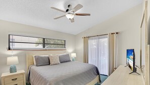 A bedroom with a bed, bedside tables, a ceiling fan, a window with blinds, a TV, and curtains. - Beachfront Hideaway in the heart of Key Largo! Your own private beach! (Key Largo)