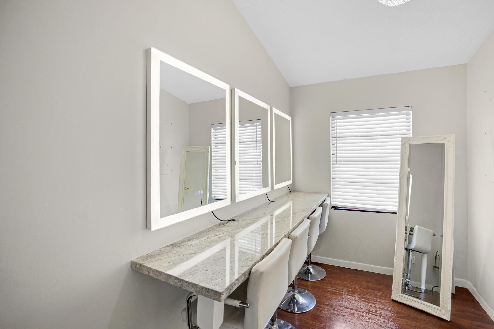A bathroom with a marble vanity, three mirrors, and a window with blinds.