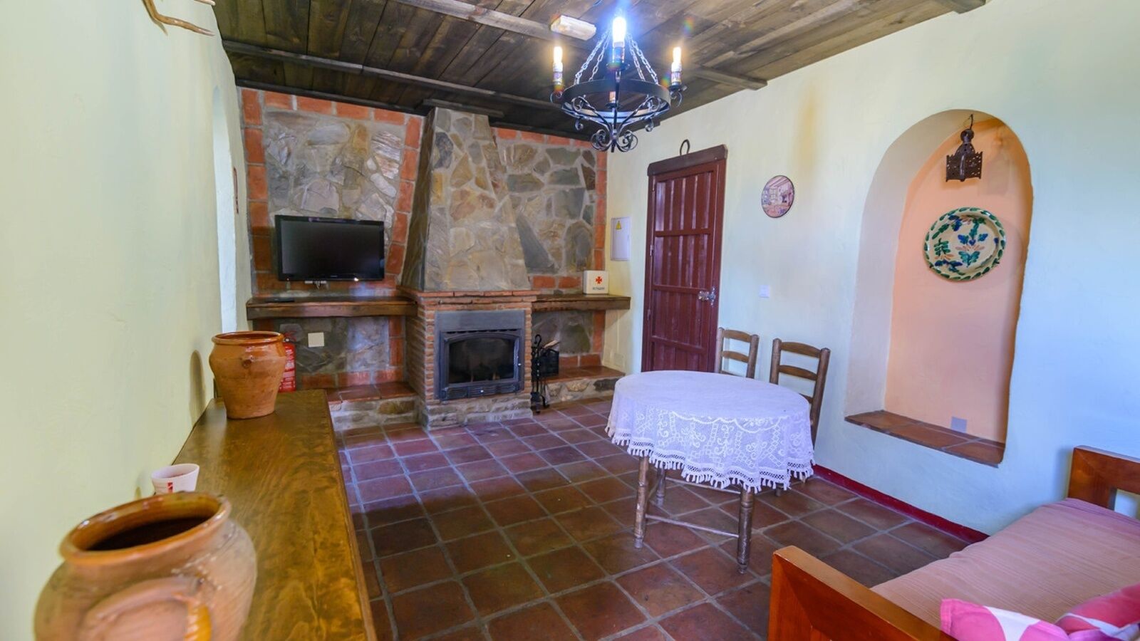 A rustic interior with a stone fireplace, a television, a dining table with chairs, and a bed.