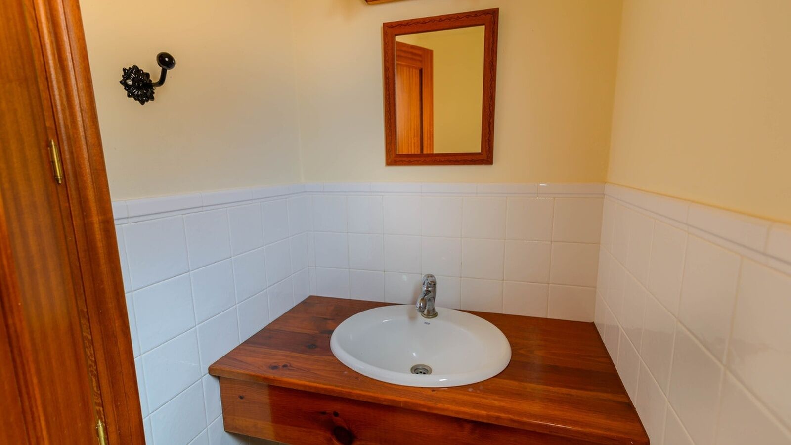 A bathroom with a wooden vanity, white tiled walls, and a mirror above the sink.
