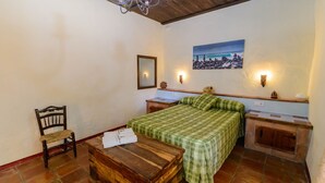 A bedroom with a bed, a wooden chair, a nightstand, a dresser, and a painting on the wall. - Casa Rural Azahar Periana by Ruralidays (Málaga)