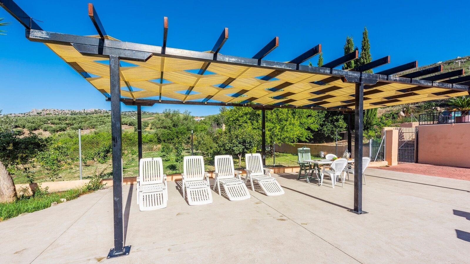 An outdoor patio with a pergola, white lounge chairs, and a table.