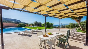 A covered outdoor area with a pool, white lounge chairs, and a table with a bottle and fruit. - Casa Rural Azahar Periana by Ruralidays (Málaga)