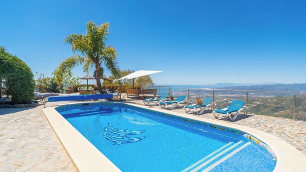 A swimming pool with lounge chairs, a palm tree, and a view of the landscape.
