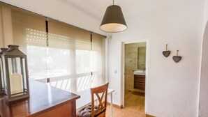 Ein Zimmer mit einem Holztisch, einem Stuhl, einer hängenden Laterne und Blick durch ein Fenster mit Jalousien.