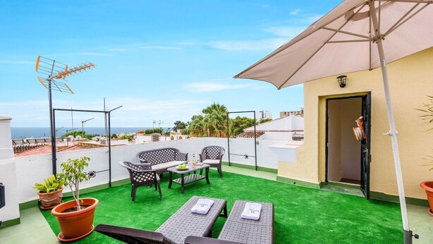 Eine Dachterrasse mit künstlichem Rasen, zwei Liegestühlen, einem Tisch und einem großen Sonnenschirm.