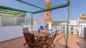 Um terraço no telhado com uma mesa e cadeiras, um relógio e uma torre de sino ao fundo.