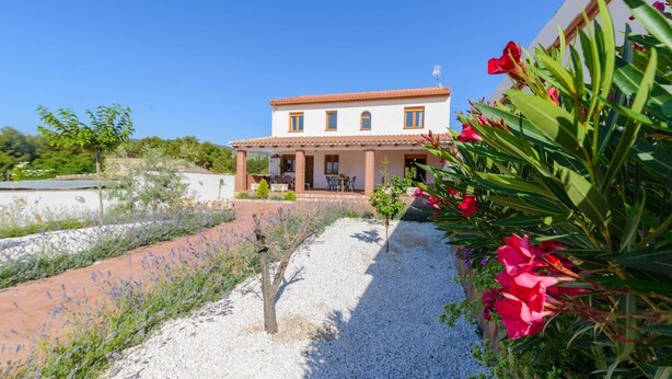 A two-story house with a patio and a gravel pathway. - Casa Rural Embalse Bermejales Arenas del Rey by Ruralidays (Granada)