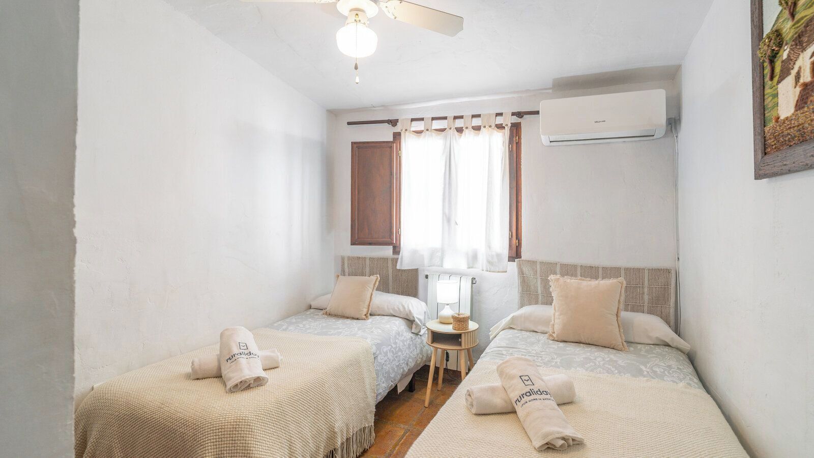 A small, cozy bedroom with two beds, a nightstand, a lamp, and an air conditioning unit.