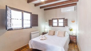 Ein Schlafzimmer mit Bett, Heizkörper, einem Fenster mit Rollläden, einem Nachttisch mit Lampe und einer Wand-Klimaanlage.