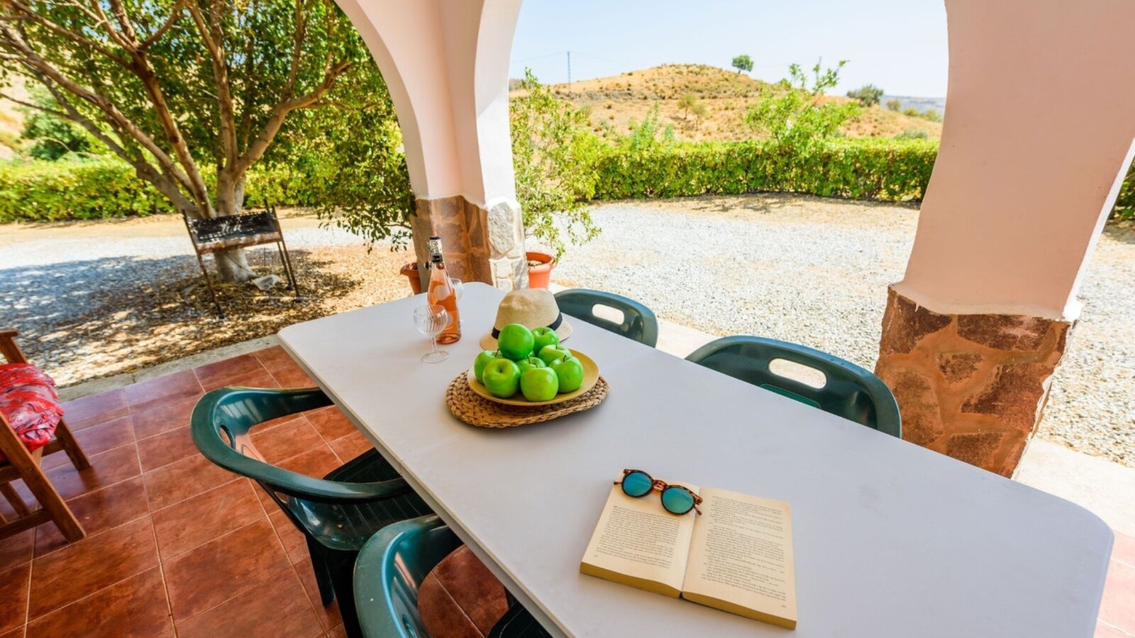 Une table dressée à l’extérieur, avec un livre, des lunettes et un panier de pommes vertes.