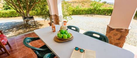 Une table dressée à l’extérieur, avec un livre, des lunettes et un panier de pommes vertes.
